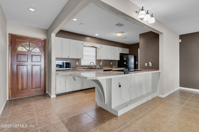 kitchen with visible vents, freestanding refrigerator, a sink, white cabinets, and stainless steel microwave