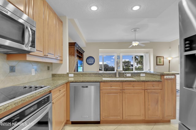 kitchen featuring decorative backsplash, a peninsula, stainless steel appliances, a ceiling fan, and a sink