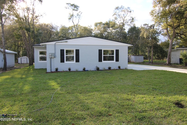 single story home featuring a storage shed, an outbuilding, a front lawn, and stucco siding