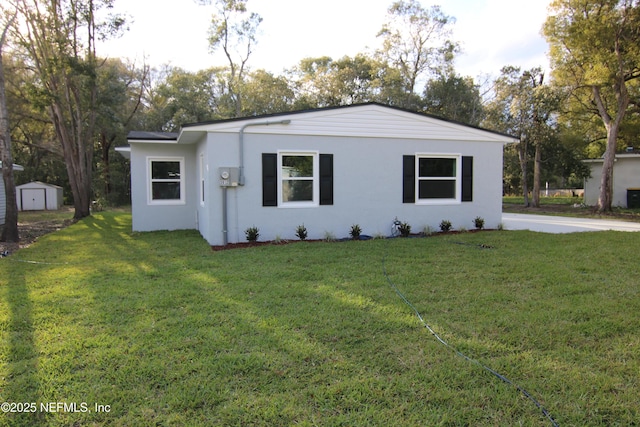 view of front facade with stucco siding, a storage shed, an outdoor structure, and a front lawn