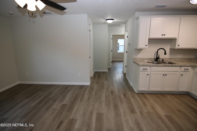 kitchen featuring visible vents, wood finished floors, white cabinets, a textured ceiling, and a sink