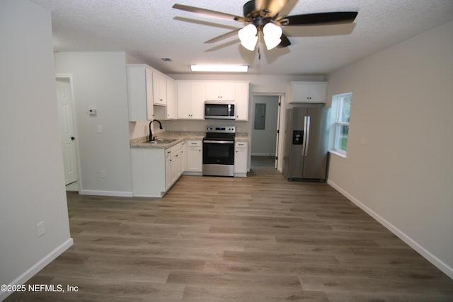 kitchen with electric panel, appliances with stainless steel finishes, a textured ceiling, white cabinetry, and a sink