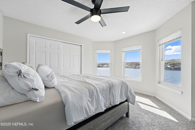 carpeted bedroom featuring a ceiling fan, baseboards, a closet, and a textured ceiling