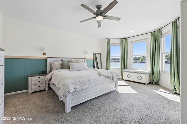 carpeted bedroom with a wainscoted wall, a water view, and ceiling fan