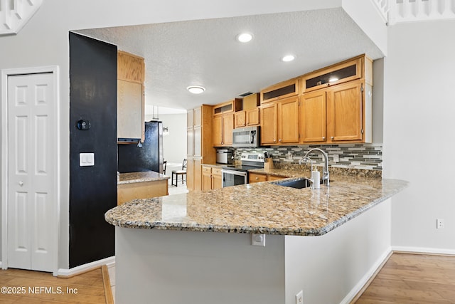 kitchen featuring a peninsula, light wood-style flooring, a sink, stainless steel appliances, and tasteful backsplash