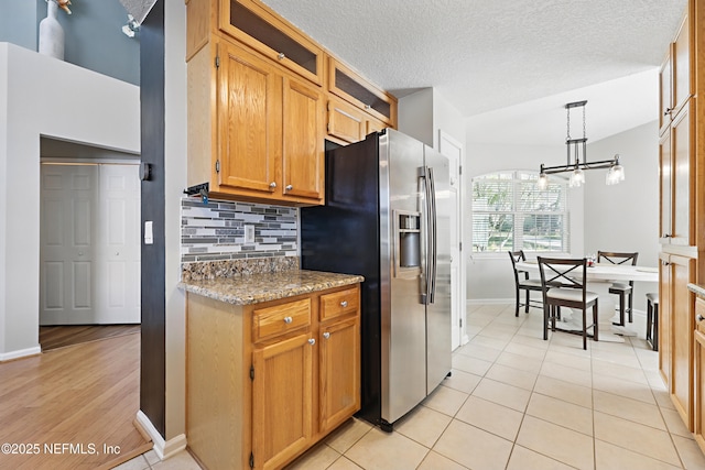 kitchen featuring tasteful backsplash, stainless steel fridge with ice dispenser, light tile patterned floors, hanging light fixtures, and a textured ceiling