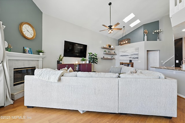 living room with a tiled fireplace, high vaulted ceiling, wood finished floors, and ceiling fan