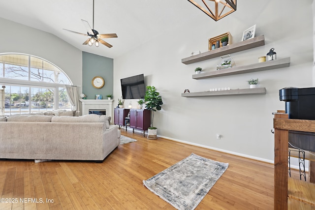 living area with a glass covered fireplace, baseboards, hardwood / wood-style floors, and ceiling fan