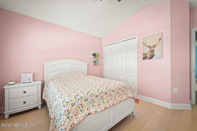 bedroom with a closet, baseboards, light wood-style floors, and vaulted ceiling