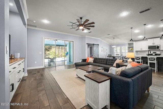 living area with visible vents, ceiling fan, dark wood finished floors, a barn door, and a textured ceiling