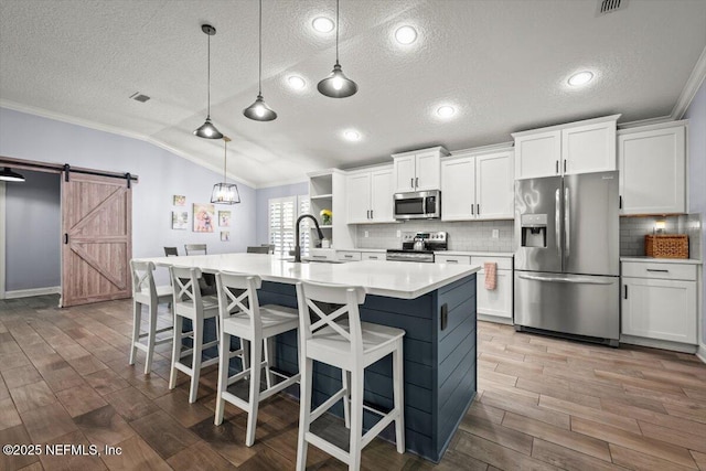 kitchen featuring lofted ceiling, a sink, stainless steel appliances, crown molding, and a barn door