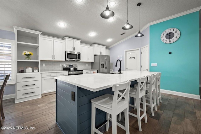 kitchen featuring crown molding, vaulted ceiling, appliances with stainless steel finishes, dark wood-style floors, and a kitchen island with sink