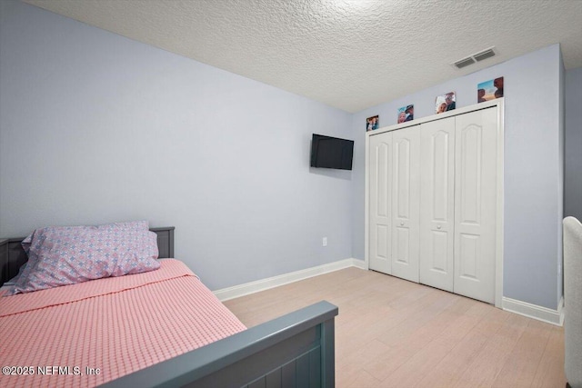 bedroom with visible vents, baseboards, light wood-type flooring, a closet, and a textured ceiling