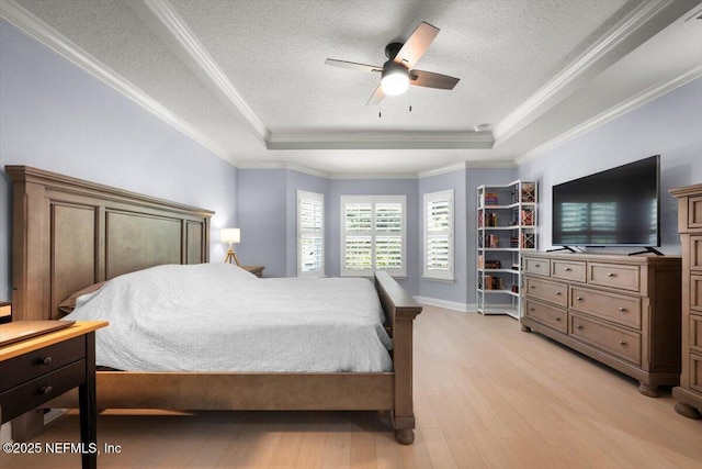 bedroom with a tray ceiling, crown molding, light wood finished floors, and a textured ceiling