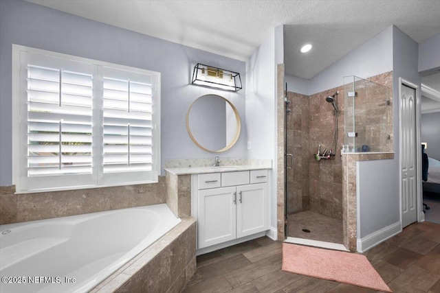 bathroom featuring a stall shower, a textured ceiling, wood finished floors, a bath, and vanity