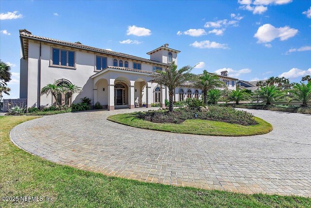 mediterranean / spanish-style home with curved driveway, a tiled roof, a front lawn, and stucco siding