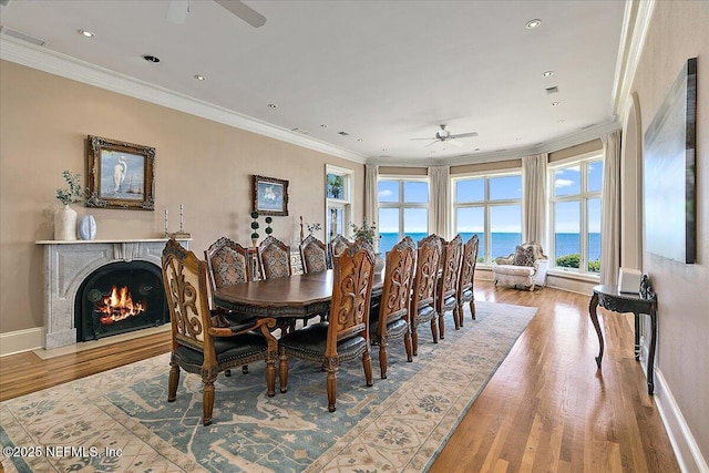 dining room with baseboards, a lit fireplace, ornamental molding, light wood-style flooring, and a ceiling fan