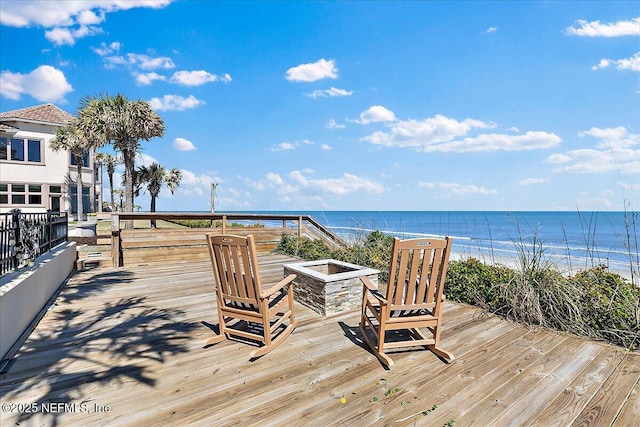 wooden deck featuring an outdoor fire pit, a view of the beach, and a water view