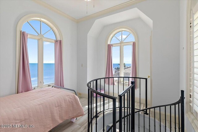 bedroom featuring light wood finished floors, crown molding, baseboards, and a water view