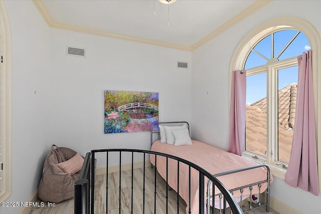 bedroom featuring visible vents, baseboards, wood finished floors, and crown molding