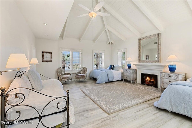 bedroom with beamed ceiling, multiple windows, wood finished floors, and a warm lit fireplace