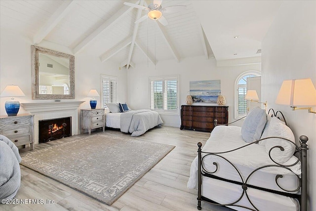 bedroom with lofted ceiling with beams, a warm lit fireplace, wood finished floors, and ceiling fan