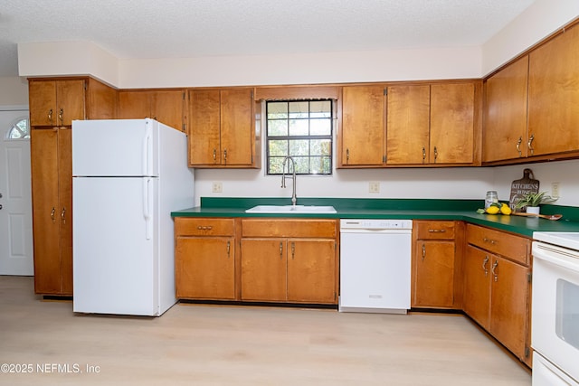 kitchen featuring a sink, white appliances, a textured ceiling, and brown cabinetry