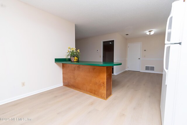 kitchen featuring baseboards, visible vents, a peninsula, freestanding refrigerator, and light wood-type flooring