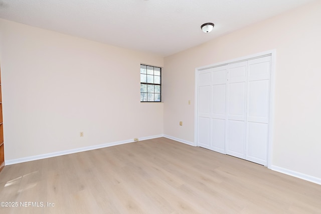 unfurnished bedroom featuring baseboards, a closet, and light wood-type flooring