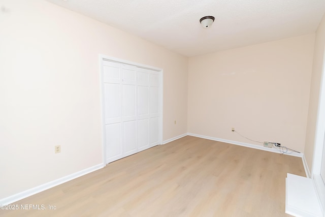 unfurnished bedroom with light wood-style flooring, baseboards, a closet, and a textured ceiling