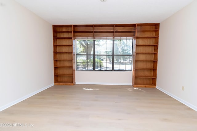 unfurnished room with built in shelves, baseboards, and light wood-style flooring