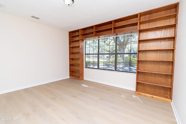 empty room with light wood finished floors, visible vents, built in shelves, and baseboards