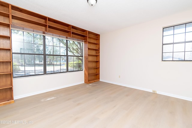 empty room with built in shelves, baseboards, light wood finished floors, and a textured ceiling