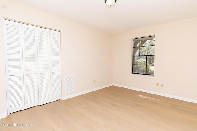 unfurnished bedroom featuring a closet, visible vents, baseboards, and wood finished floors