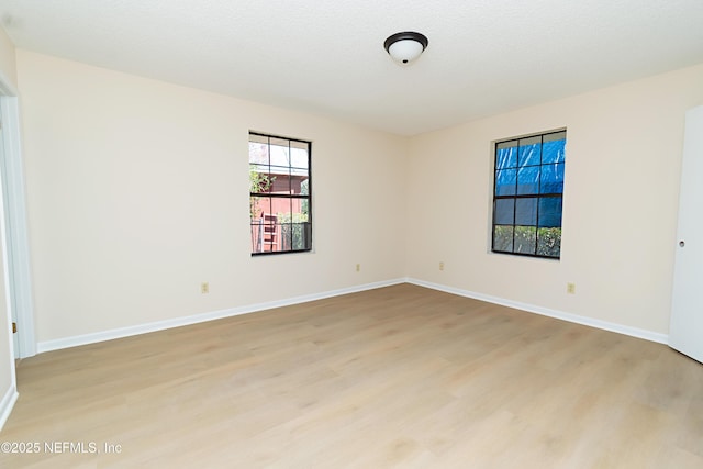 empty room featuring baseboards, light wood finished floors, and a textured ceiling