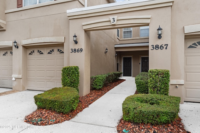 view of exterior entry with an attached garage and stucco siding