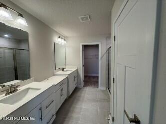 full bathroom featuring tile patterned flooring, double vanity, an enclosed shower, and a sink