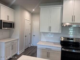 kitchen with light countertops, under cabinet range hood, appliances with stainless steel finishes, white cabinetry, and backsplash