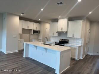 kitchen featuring dark wood-style floors, a kitchen island with sink, a sink, black electric range, and under cabinet range hood