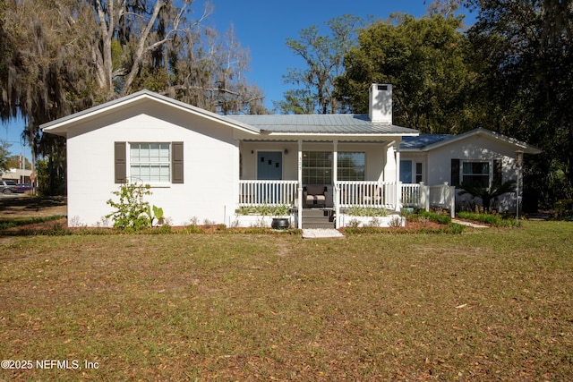 ranch-style home with a chimney, a porch, concrete block siding, and a front yard