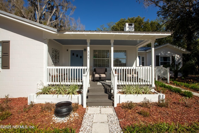 entrance to property featuring a porch, concrete block siding, a chimney, and metal roof