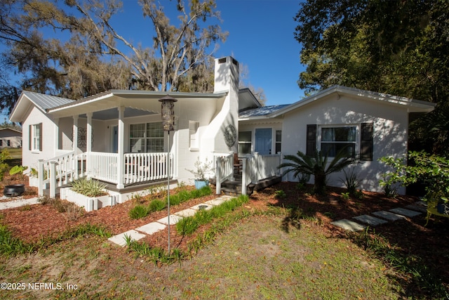 view of front of property with a porch, a chimney, and metal roof