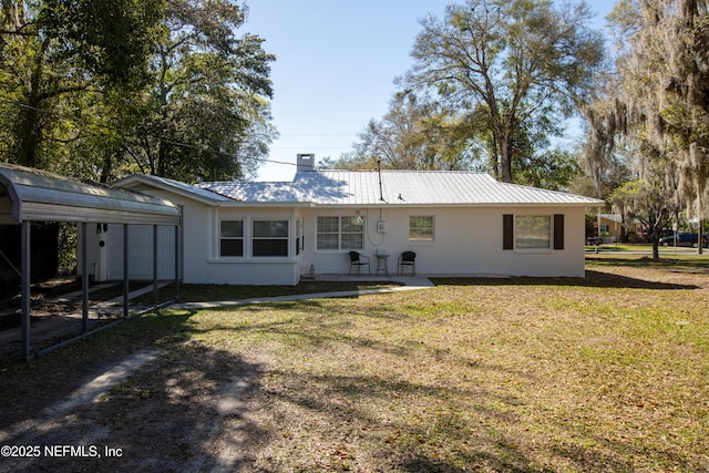 back of house featuring metal roof, a carport, a chimney, and a yard