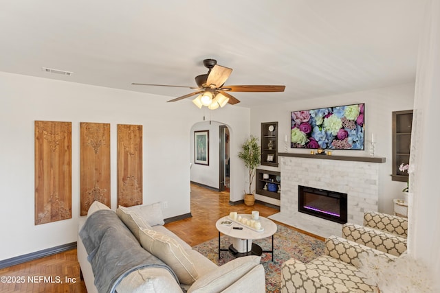 living area with visible vents, baseboards, a fireplace, arched walkways, and ceiling fan