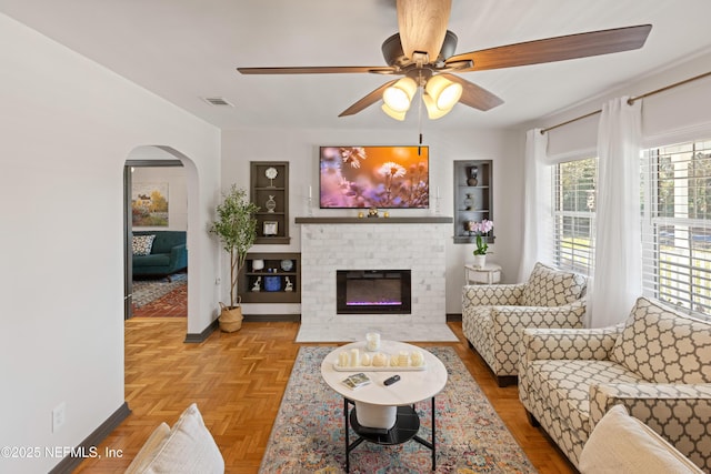 living room featuring a ceiling fan, visible vents, baseboards, a fireplace, and arched walkways