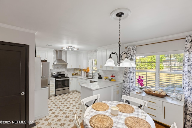 kitchen with wall chimney range hood, light floors, ornamental molding, stainless steel appliances, and a sink