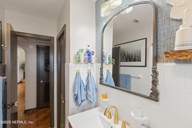 bathroom with visible vents, wainscoting, tile walls, and a sink