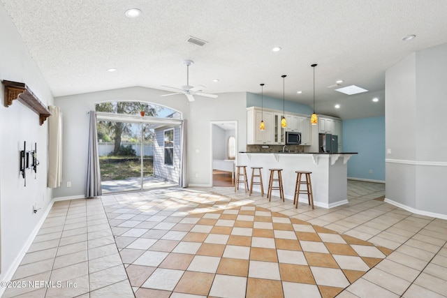 kitchen with visible vents, a kitchen bar, stainless steel appliances, light tile patterned floors, and vaulted ceiling