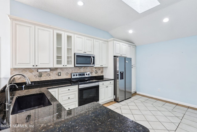 kitchen with light tile patterned floors, a sink, decorative backsplash, stainless steel appliances, and lofted ceiling with skylight