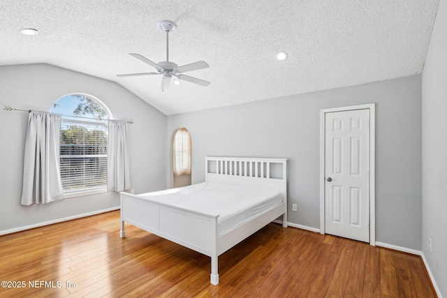 bedroom featuring baseboards, lofted ceiling, wood finished floors, a textured ceiling, and a ceiling fan